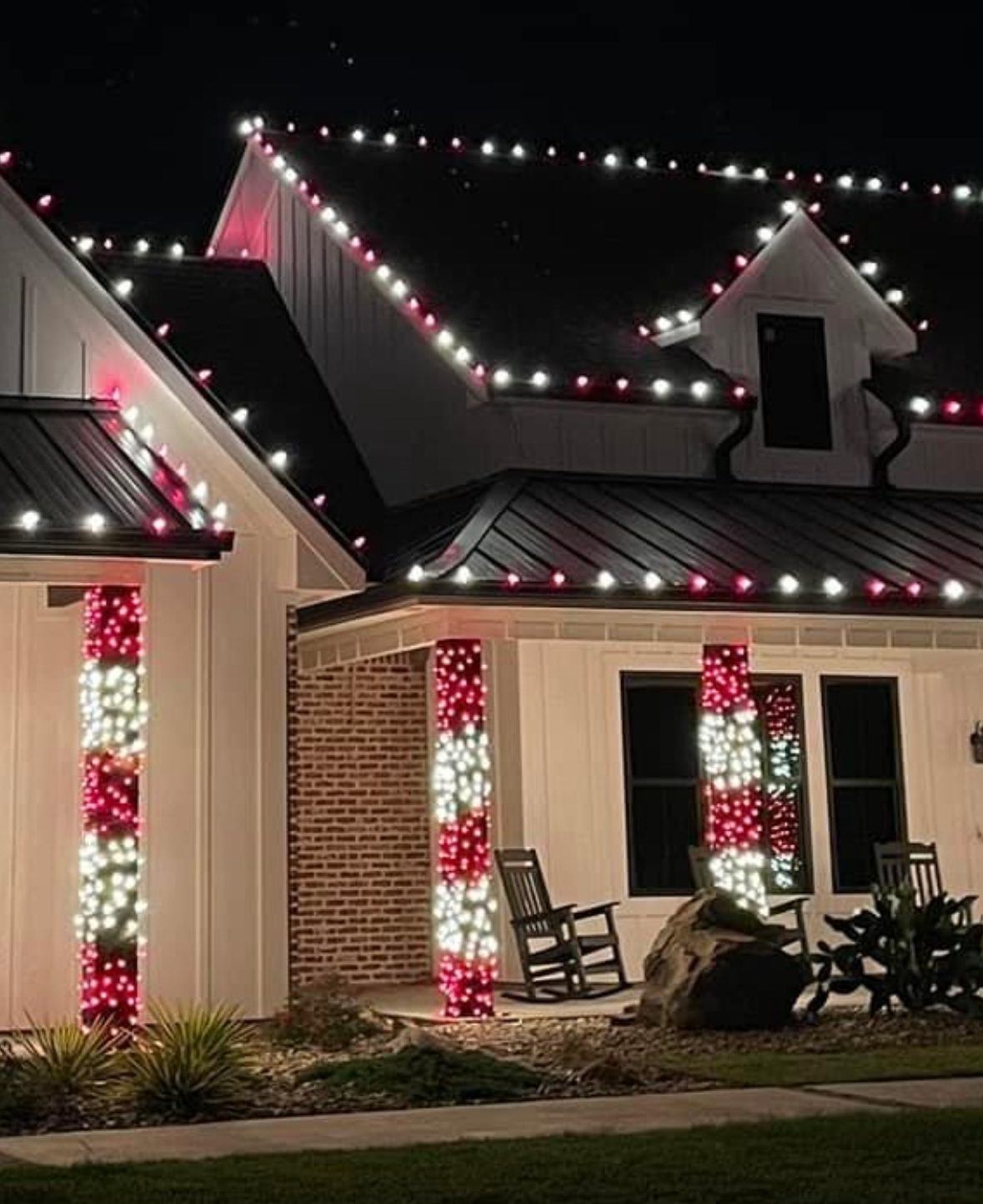 White farmhouse lit at night with red and white C9 roofline lights and porch columns wrapped like candy canes, installed by Very Good Christmas Lights
