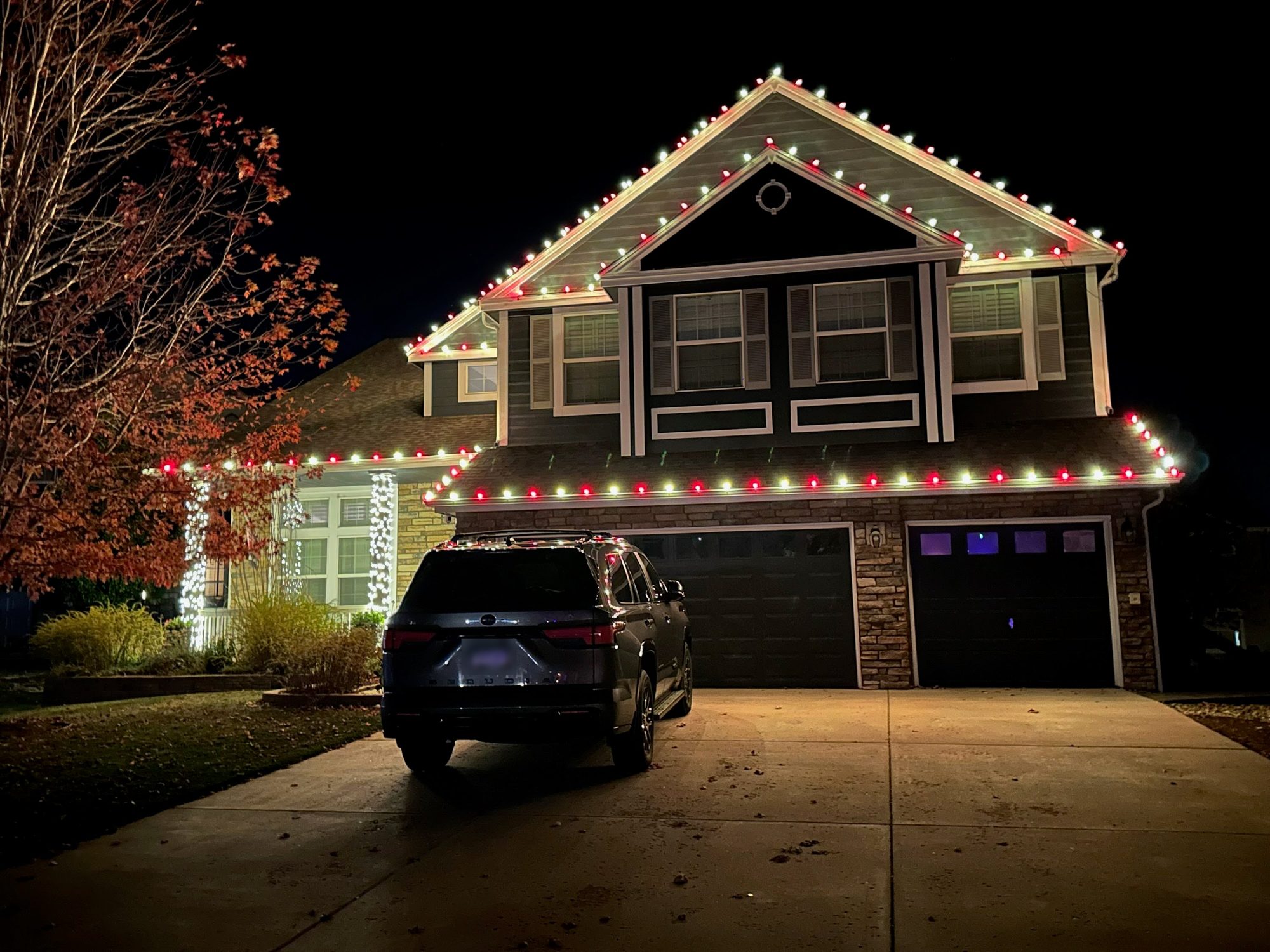 Two-story home at night with alternating red and white C9 bulbs outlining the roofline and gables, plus white-wrapped porch columns