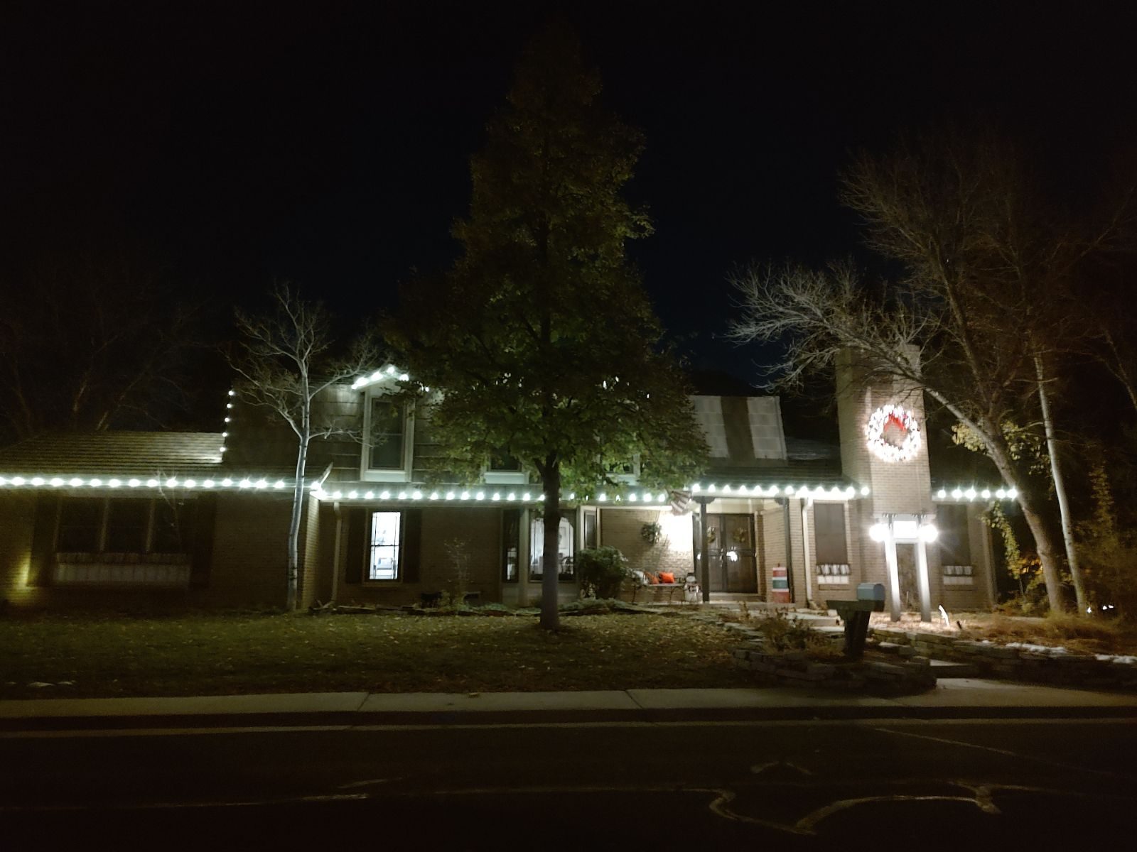 Ranch-style home at night with a warm white roofline and a lighted wreath on the brick chimney